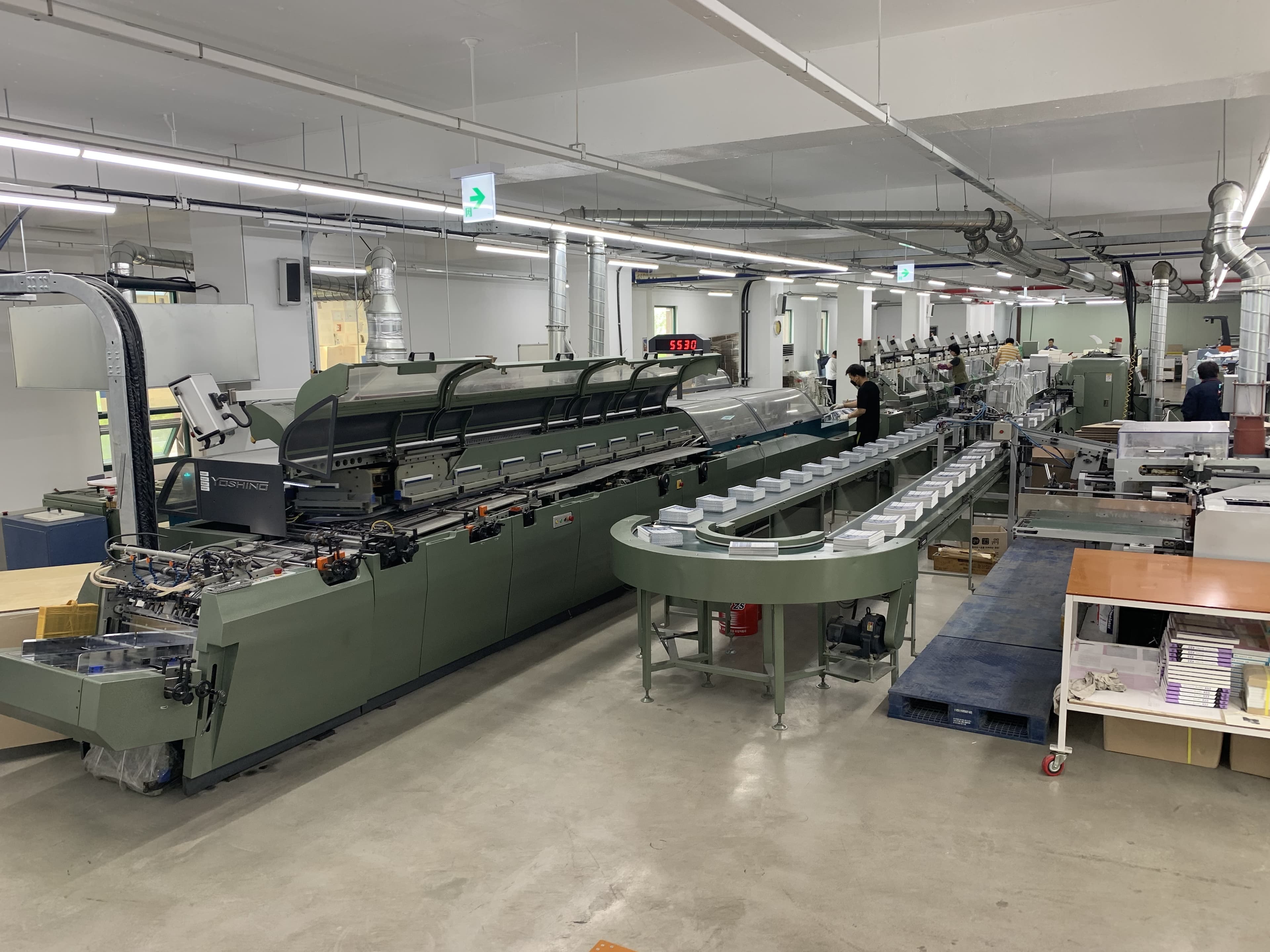 Automated binding line with finished books moving down the conveyor at Printseoul's production facility